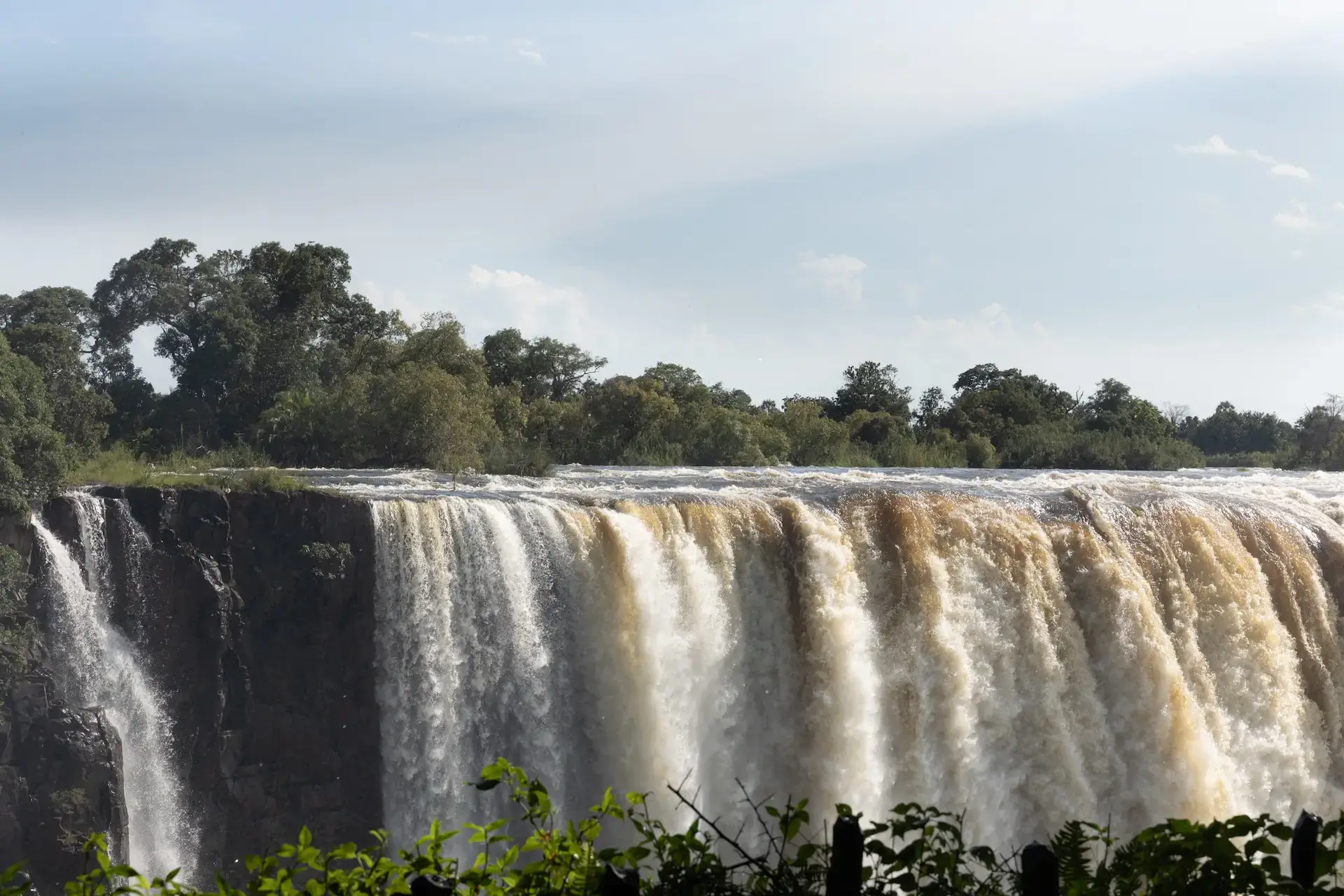 The Victoria Falls waterfall leading to the Zambezi River on a sunny day.
